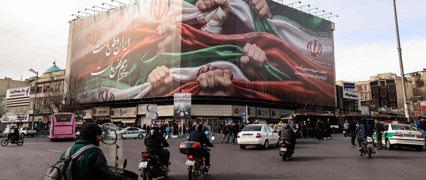 Vehicles pass by a large patriotic banner depicting the Iranian flag on Enghelab Square, Tehran, Iran, Jan. 14, 2026. (AFP Photo)