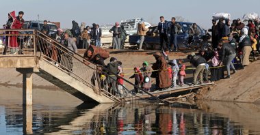 People, along with their belongings, walk across a damaged bridge as they flee from a PKK/YPG-controlled area, Rasm al-Harmal, east of Aleppo, Syria, Jan. 15, 2026. (AFP Photo)
