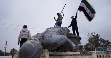 A man holds a Syrian flag as a group of civilians smash a statue of a SDF fighter in the city of Tabqa after the Syrian army took control of it, in Tabqa, Syria, Jan. 18, 2026. (Reuters Photo)