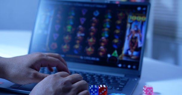 A man plays online slot games on a laptop, with gambling chips and dice nearby. (Shutterstock Photo)