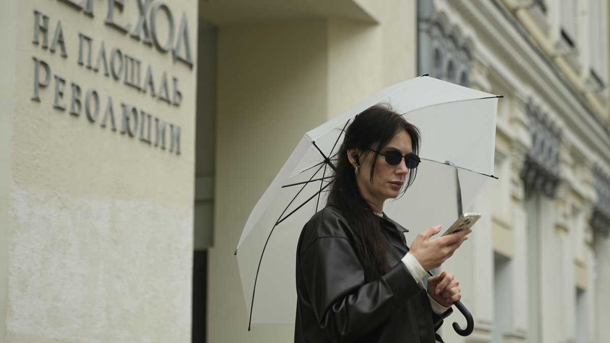 A woman checks her phone while holding an umbrella during light rain in Moscow, Russia, May 19, 2025. (AP Photo)