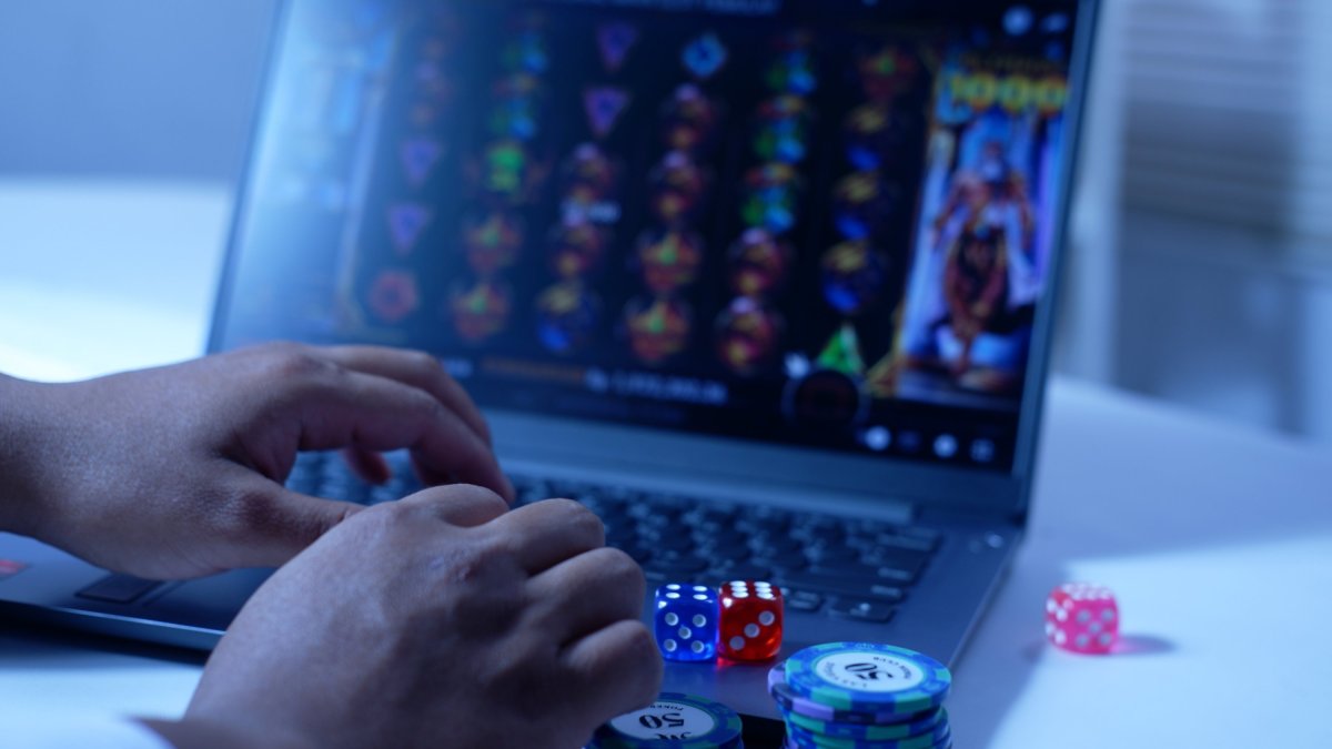A man plays online slot games on a laptop, with gambling chips and dice nearby. (Shutterstock Photo)