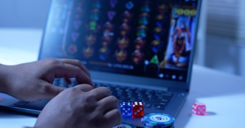 A man plays online slot games on a laptop, with gambling chips and dice nearby. (Shutterstock Photo)
