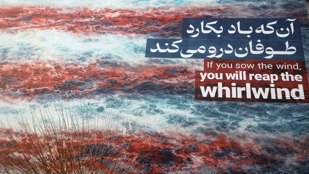 In a giant poster featuring an image of the American flag in blood targeting an American aircraft carrier, the phrase “He who sows the wind shall reap the whirlwind” appears in English and Persian, Revolution Square, Tehran, Iran, Jan. 25, 2026. (AA Photo)