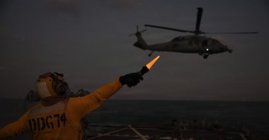 A US Navy technician onboard USS McFaul directs an MH-60S Sea Hawk helicopter during nighttime flight operations in the Arabian Gulf, Jan. 30, 2026. (AFP Photo)