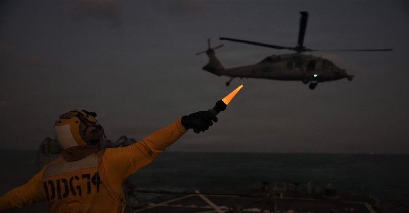 A US Navy technician onboard USS McFaul directs an MH-60S Sea Hawk helicopter during nighttime flight operations in the Arabian Gulf, Jan. 30, 2026. (AFP Photo)
