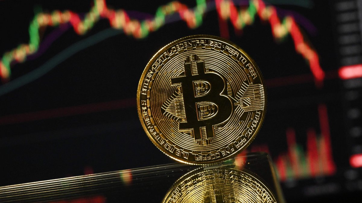 A gold-plated souvenir bitcoin coin is reflected in a mirror and arranged for a photograph in front of a computer screen displaying the bitcoin monthly price chart in a residential property in Guildford, south of London, U.K., Nov. 22, 2025. (AFP Photo)