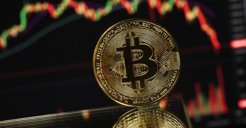 A gold-plated souvenir bitcoin coin is reflected in a mirror and arranged for a photograph in front of a computer screen displaying the bitcoin monthly price chart in a residential property in Guildford, south of London, U.K., Nov. 22, 2025. (AFP Photo)