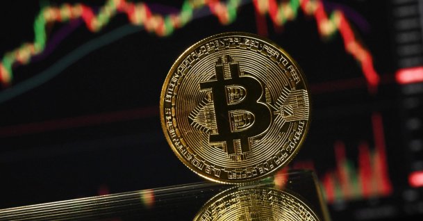 A gold-plated souvenir bitcoin coin is reflected in a mirror and arranged for a photograph in front of a computer screen displaying the bitcoin monthly price chart in a residential property in Guildford, south of London, U.K., Nov. 22, 2025. (AFP Photo)