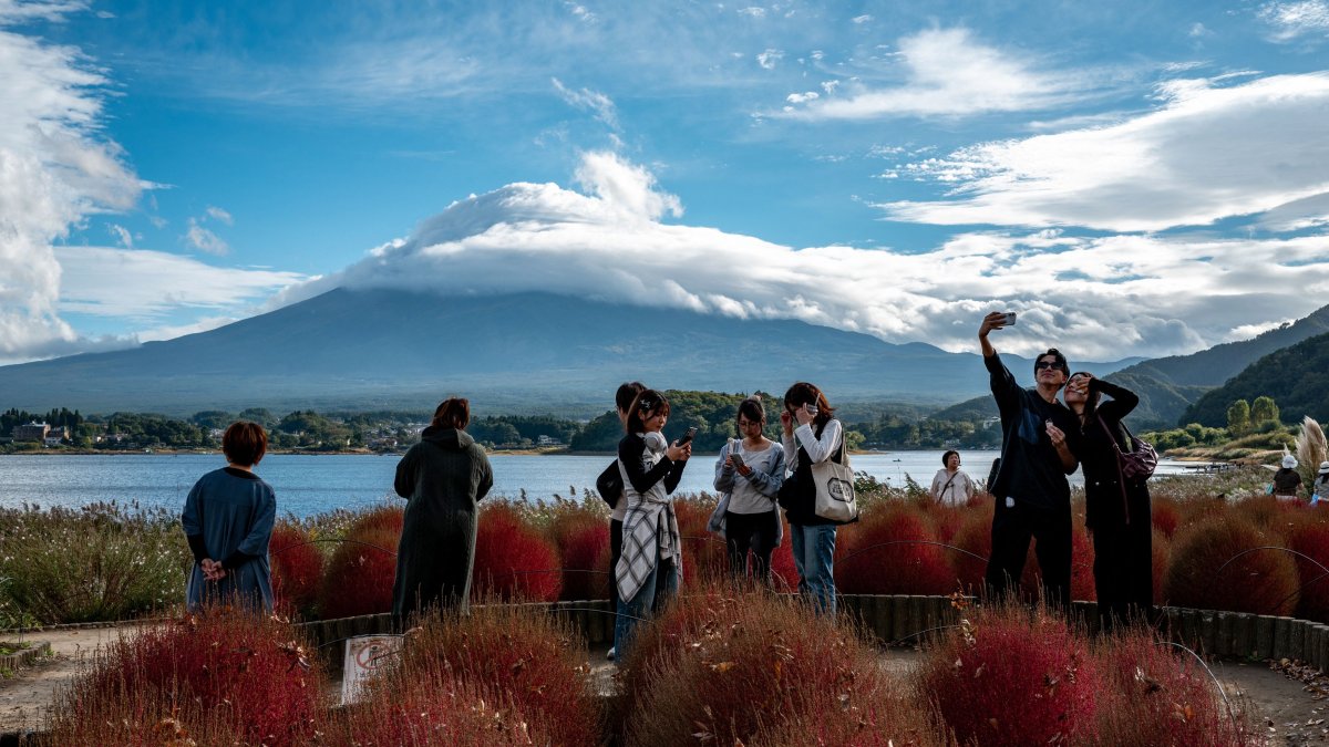 Tourists take pictures as cloud-clad Mount Fuji is seen in the background from Oishi park in the town of Fujikawaguchiko, Yamanashi Prefecture, Japan, Oct. 18, 2025. (AFP Photo)