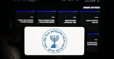 The undated photo shows a person holding mobile phone with logo of Israeli national intelligence agency Mossad in front of web page. (Shutterstock Photo)