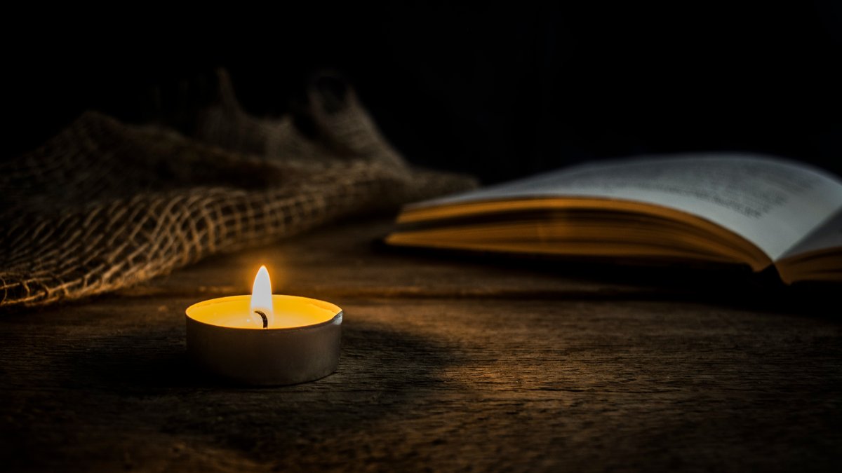 Warm candlelight next to an open book on a rustic wooden table in a dark setting. Perfect for concepts like peace, meditation, reading or vintage mood. (Shutterstock Photo)
