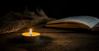 Warm candlelight next to an open book on a rustic wooden table in a dark setting. Perfect for concepts like peace, meditation, reading or vintage mood. (Shutterstock Photo)