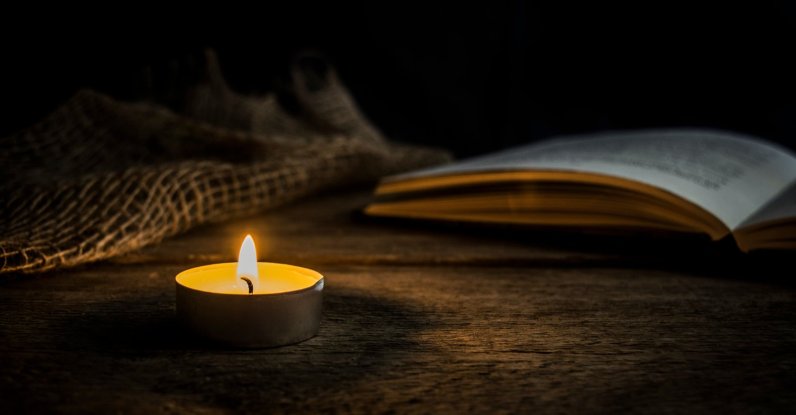 Warm candlelight next to an open book on a rustic wooden table in a dark setting. Perfect for concepts like peace, meditation, reading or vintage mood. (Shutterstock Photo)