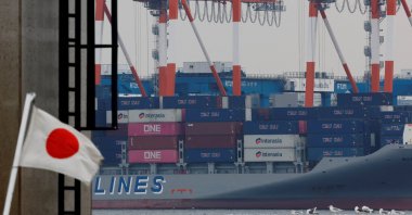 A Japanese national flag flutters in front of cargo containers at an industrial port, Tokyo, Japan, Feb. 16, 2026. (Reuters Photo)