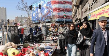 Iranians walk past a street vendor's stand with an anti-U.S. billboard visible in the background, in Tehran, Iran, Feb. 17, 2026. (AFP Photo)