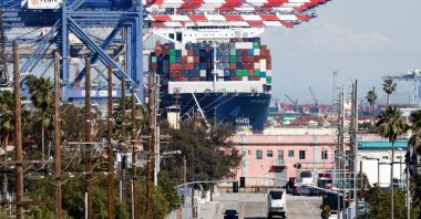 A container ship floats loaded with shipping containers at the Port of Los Angeles as vehicles drive nearby in Los Angeles, California, U.S., Feb. 20, 2026. (AFP Photo)