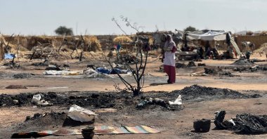 A displaced Sudanese woman who left el-Fasher after its fall with others, walks amid the remains of a fire that broke out at a camp in Tawila, Sudan, Feb. 11, 2026. (AFP Photo)