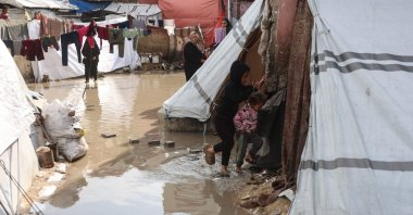 Children make their way through a waterlogged alley at a makeshift camp sheltering displaced Palestinians in Khan Younis, southern Gaza Strip, Feb. 24, 2026. (AFP Photo)