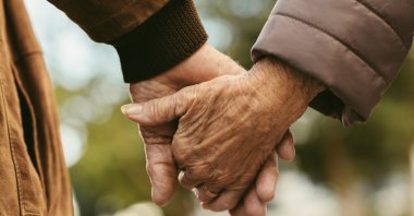 An elderly couple holding hands and walking outdoors. (Shutterstock Photo)