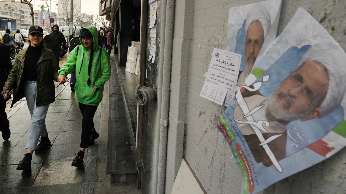 Women walk past electoral posters of Ayatollah Alireza Arafi, in downtown Tehran, Iran, Feb. 21, 2024. (AP Photo)