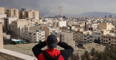 A man looks through binoculars as a plume of smoke rises after a military strike on the capital Tehran, Iran, March 2, 2026. (AFP Photo)