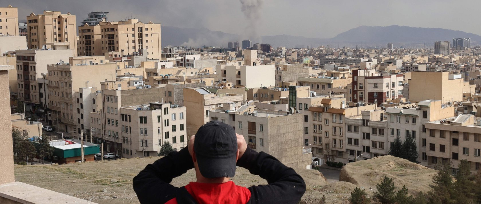 A man looks through binoculars as a plume of smoke rises after a military strike on the capital Tehran, Iran, March 2, 2026. (AFP Photo)