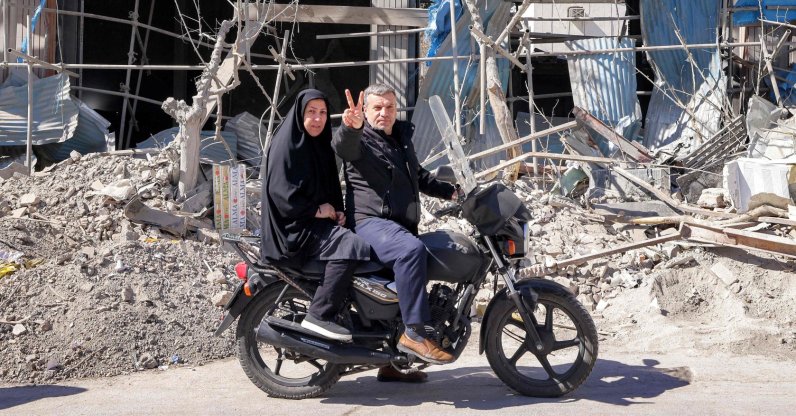 A man reacts while riding a motorcycle past buildings collapsed and damaged in U.S.-Israeli strikes near Ferdowsi Square in Tehran, Iran, March 3, 2026. (AFP Photo)