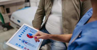 A doctor consults with an overweight patient, reviewing test results. (Shutterstock Photo)