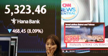 A currency dealer works in front of an electronic board displaying the Korea Composite Stock Price Index (KOSPI) and a news report on the U.S.-Israeli conflict with Iran, Seoul, South Korea, March 4, 2026. (Reuters Photo)