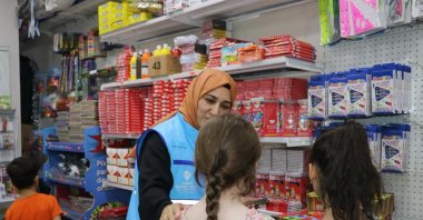 A Türkiye Diyanet Foundation team member helps orphaned children buy stationery during a school support activity, Türkiye, March 5, 2026. (AA Photo)