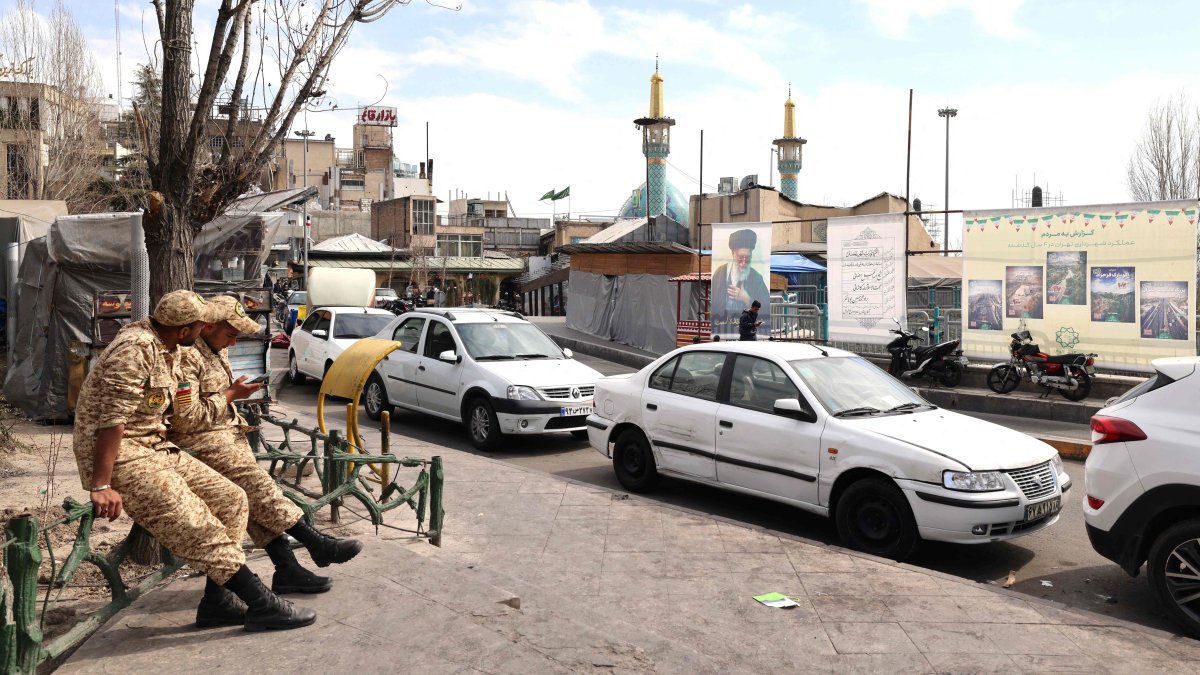 Two Iranian soldiers look at their mobile phone as they sit close to an image of Iran&amp;#039;s slain supreme leader Ayatollah Ali Khamenei (R), along a street close to Tajrish Square in Tehran, Iran, March 7, 2026. (AFP Photo)