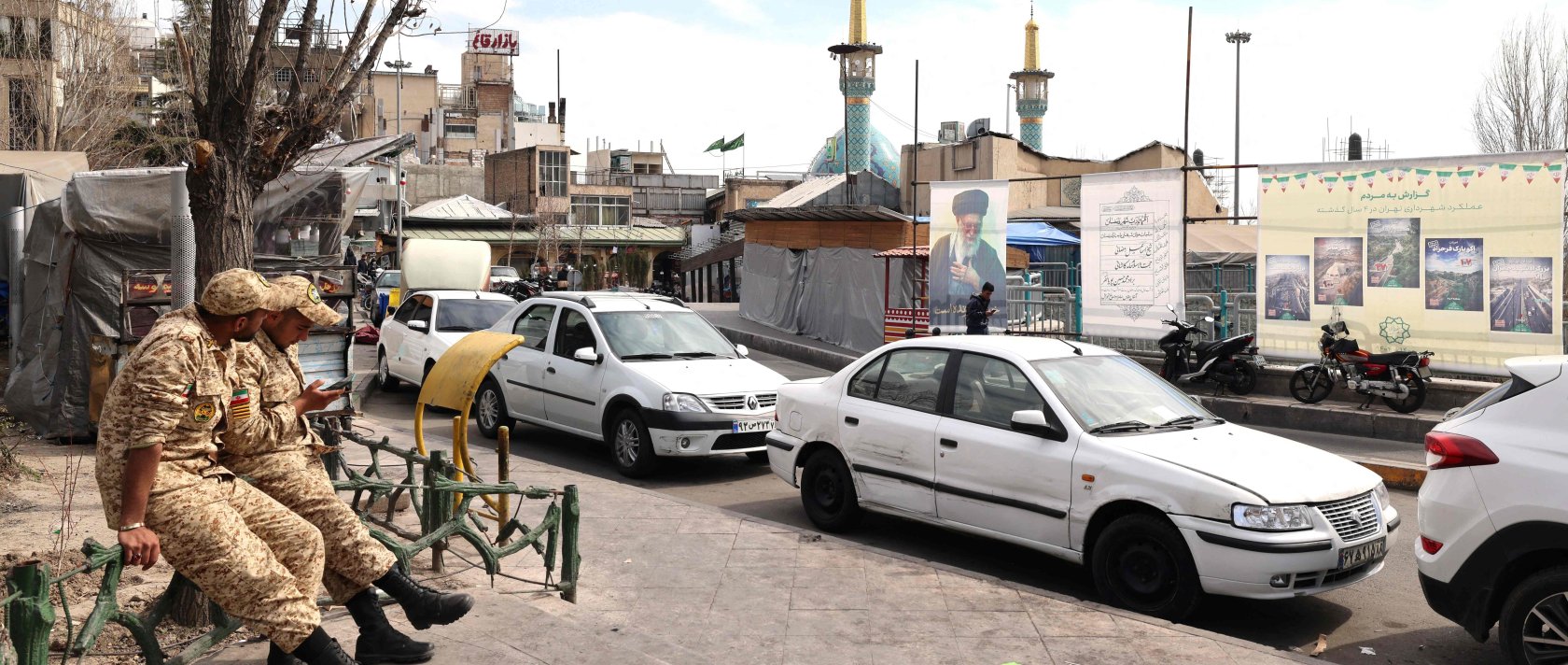 Two Iranian soldiers look at their mobile phone as they sit close to an image of Iran&amp;#039;s slain supreme leader Ayatollah Ali Khamenei (R), along a street close to Tajrish Square in Tehran, Iran, March 7, 2026. (AFP Photo)