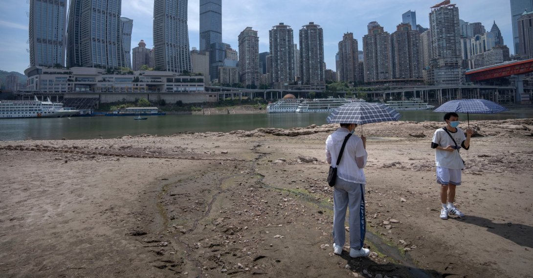 Students carrying umbrellas stand on the dry riverbed of the Jialing Rivera, a tributary of the Yangtze, Chongqing, China, Aug. 19, 2022. (AP Photo)