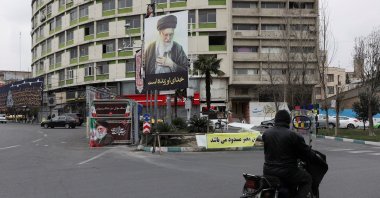 A person rides a motorcycle next to a poster of Iran's late supreme leader, Ayatollah Ali Khamenei, amid the U.S.-Israeli attacks on Iran, Tehran, Iran, March 10, 2026. (Reuters Photo)