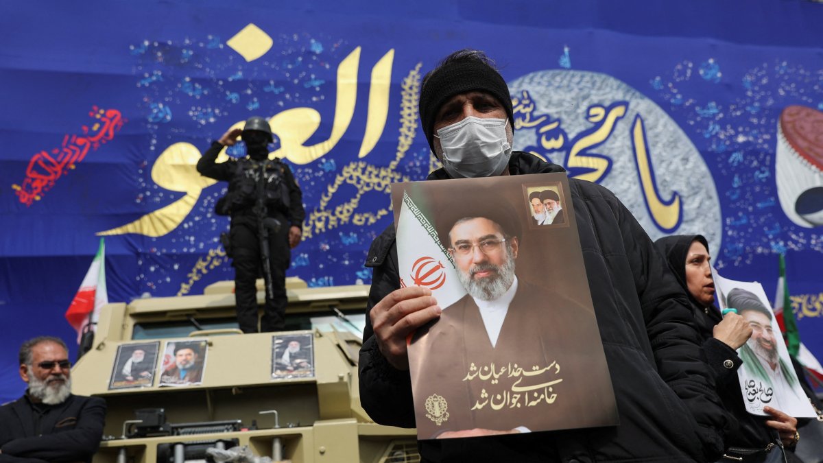 A man holds a picture of Iran's new supreme leader, Mojtaba Khamenei, while people attend a funeral ceremony for the Iranian military commanders who were killed in strikes, Tehran, Iran, March 11, 2026. (Reuters Photo)