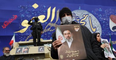 A man holds a picture of Iran's new supreme leader, Mojtaba Khamenei, while people attend a funeral ceremony for the Iranian military commanders who were killed in strikes, Tehran, Iran, March 11, 2026. (Reuters Photo)