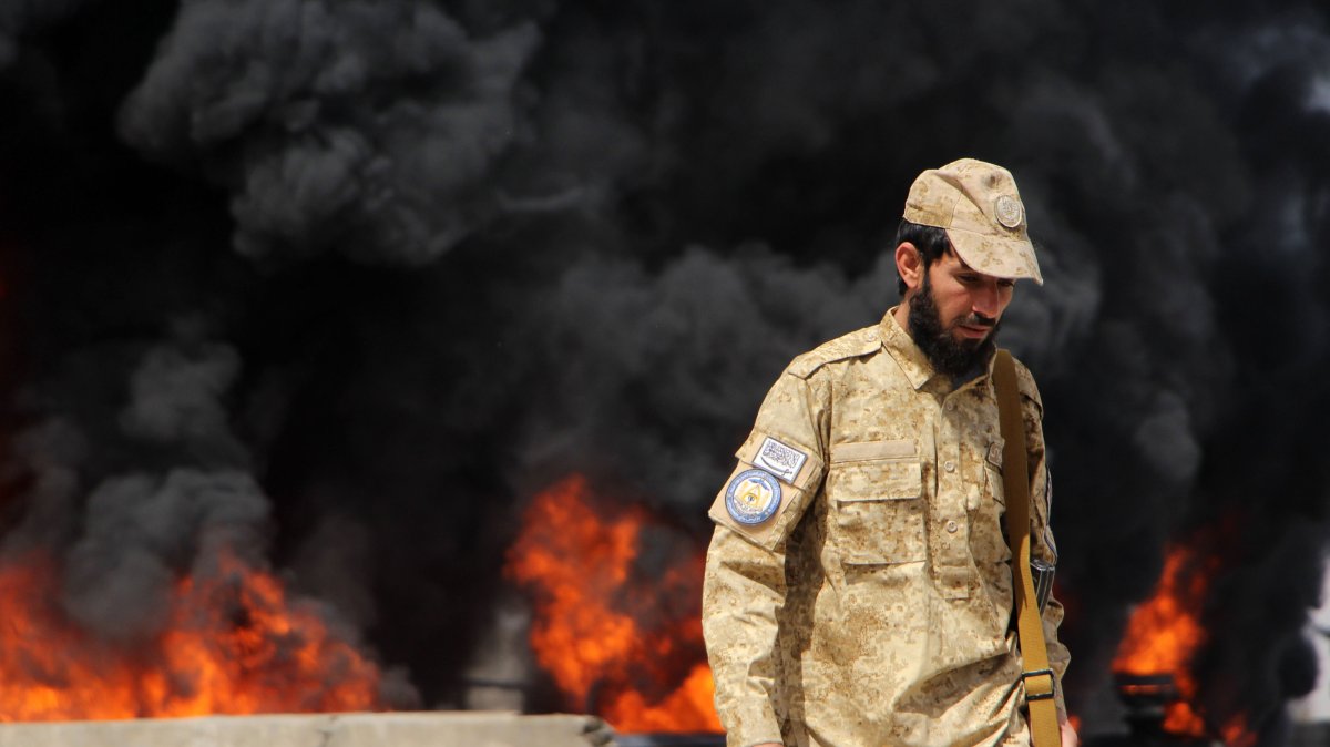 A Taliban security official stands guard as flames rise from a fuel depot allegedly hit in a Pakistani airstrike near Kandahar airport, Kandahar, Afghanistan, March 13, 2026. (EPA Photo)