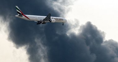 An Emirates Airbus A350 aircraft prepares for landing as a smoke plume rises from an ongoing fire at Dubai International Airport in Dubai, UAE, March 16, 2026. (AFP Photo)