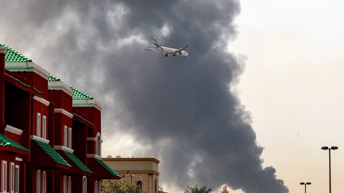 An Emirates aircraft prepares for landing as a smoke plume rises from an ongoing fire near Dubai International Airport in Dubai, March 16, 2026. (AFP Photo)
