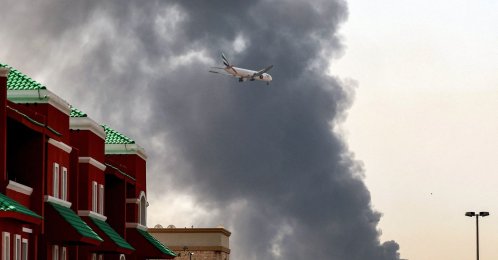 An Emirates aircraft prepares for landing as a smoke plume rises from an ongoing fire near Dubai International Airport in Dubai, March 16, 2026. (AFP Photo)