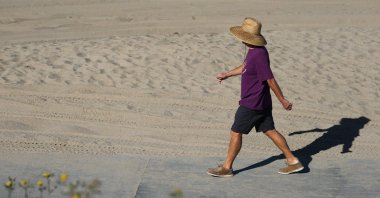 A person wears a hat for shade under the morning sun while walking along The Strand in Redondo Beach, California, U.S., March 20, 2026. (AFP Photo)