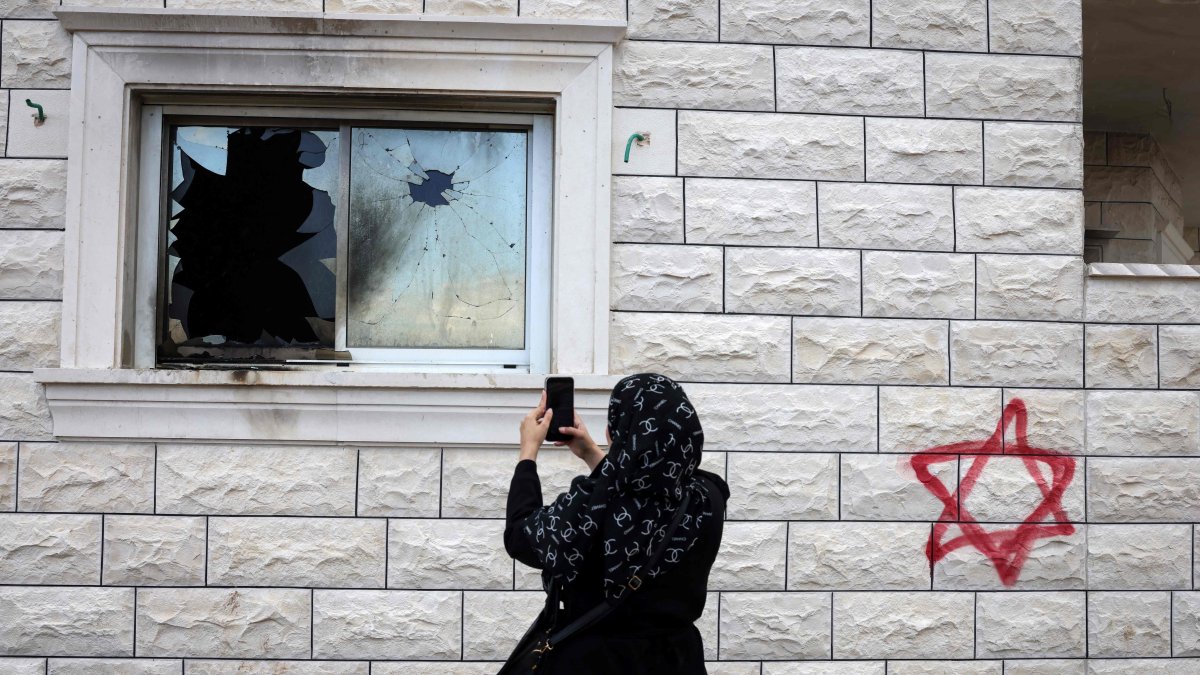 A Palestinian woman photographs a shattered window beside graffiti of a Jewish Star of David sprayed on the wall of a damaged home following a Israeli settler attack in Silat al-Dhahr, occupied West Bank, Palestine, March 22, 2026. (AFP Photo)