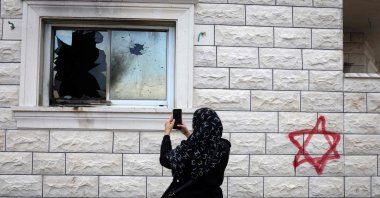 A Palestinian woman photographs a shattered window beside graffiti of a Jewish Star of David sprayed on the wall of a damaged home following a Israeli settler attack in Silat al-Dhahr, occupied West Bank, Palestine, March 22, 2026. (AFP Photo)
