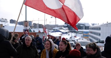 A person holds the Greenlandic flag as people stand outside a polling station during parliamentary elections, Nuuk, Greenland, Denmark, March 24, 2026. (Reuters Photo)