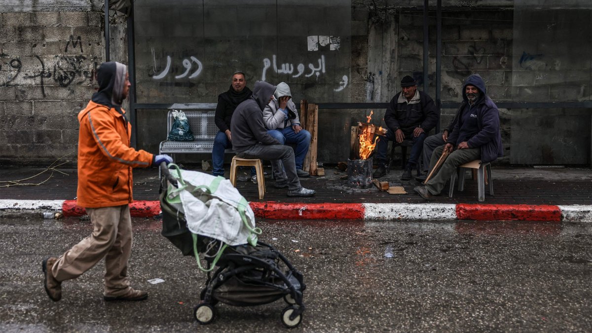 A man pushes a stroller past a group of people sitting by a fire in Hebron, in the Israeli-occupied West Bank, April 1, 2026. (AFP Photo)