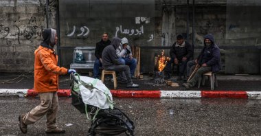 A man pushes a stroller past a group of people sitting by a fire in Hebron, in the Israeli-occupied West Bank, April 1, 2026. (AFP Photo)