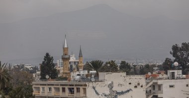 The flag of the Turkish Republic of Northern Cyprus is visible on Beşparmak (Pentadaktylos) mountain behind a mosque minaret in Lefkoşa, Feb. 12, 2024. (AFP File Photo)