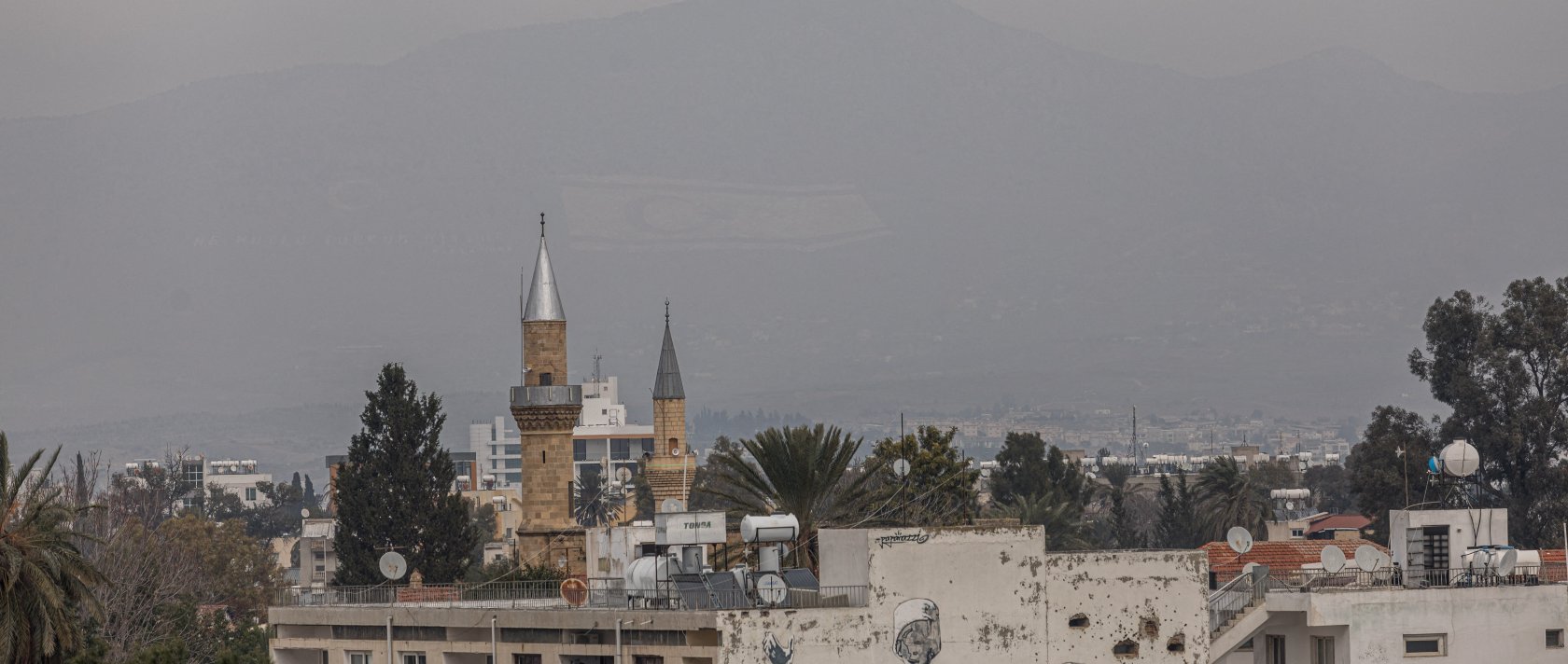 The flag of the Turkish Republic of Northern Cyprus is visible on Beşparmak (Pentadaktylos) mountain behind a mosque minaret in Lefkoşa, Feb. 12, 2024. (AFP File Photo)