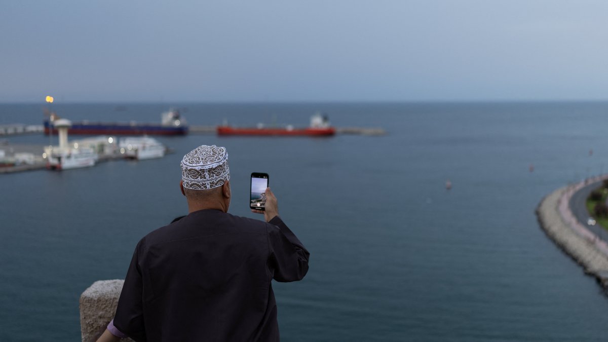 A man takes a photo with his mobile phone as vessels sit at anchor amid the U.S.-Israeli conflict with Iran, in Sultan Qaboos Port in Muscat, Oman, March 26, 2026. (Reuters Photo)